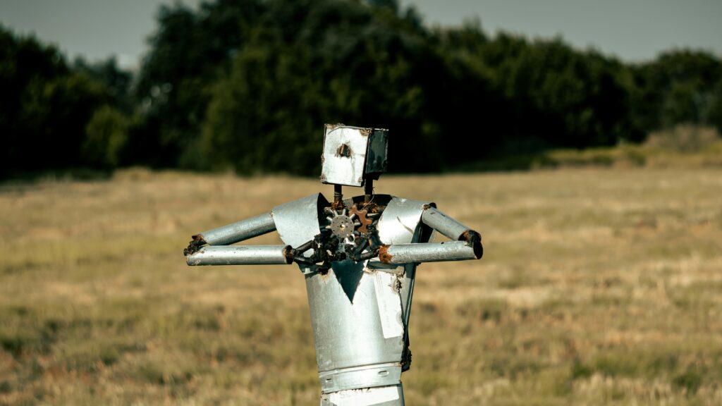 Tin man standing alone in a vast field with a backdrop of clear skies.