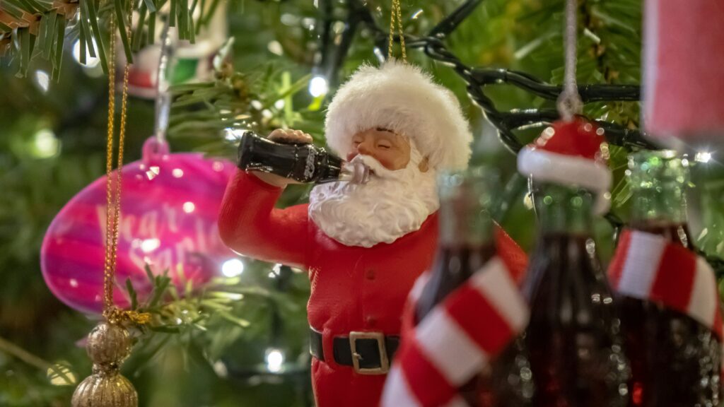 Santa Claus figurine on Christmas tree drinking from glass Coca Cola bottle.